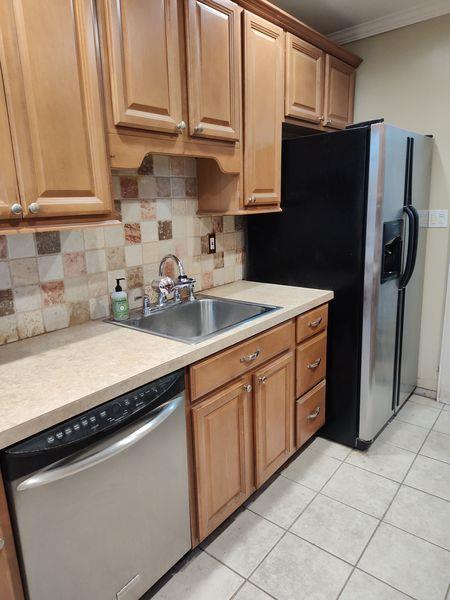 kitchen with stainless steel dishwasher, a sink, backsplash, light countertops, and crown molding