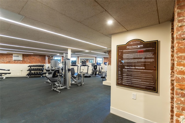 exercise room with brick wall, a wall mounted air conditioner, baseboards, and a drop ceiling