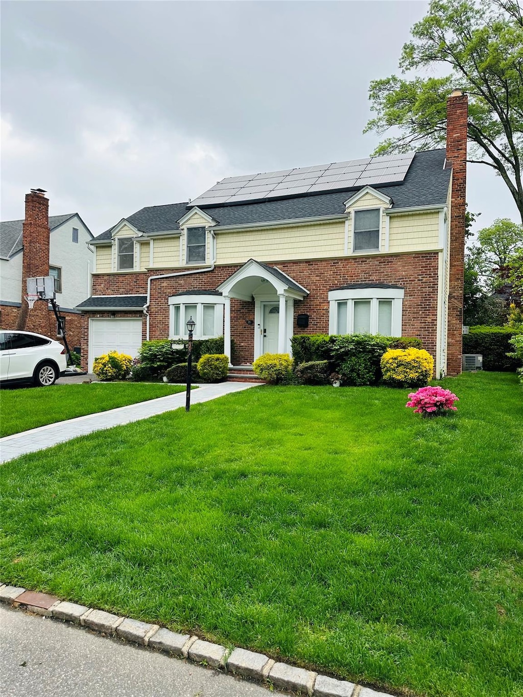 16 Andover Ln, Manhasset, NY 11030 - view of front of property featuring solar panels, a front lawn, an attached garage, and brick siding