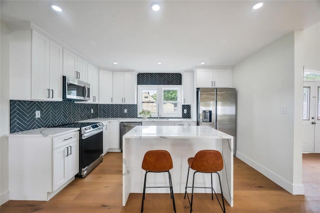205 Blueberry Ln, Hicksville, NY 11801 - kitchen with stainless steel appliances, a kitchen island, backsplash, a breakfast bar area, and light wood-type flooring
