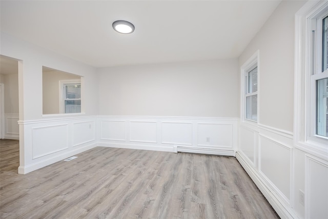 59 Burney Blvd, Mastic, NY 11950 - empty room featuring light wood-style flooring, a wainscoted wall, a decorative wall, and a baseboard heating unit