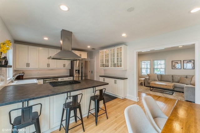 32 Henderson Ave, Port Washington, NY 11050 - kitchen featuring appliances with stainless steel finishes, island range hood, a peninsula, dark countertops, and glass insert cabinets