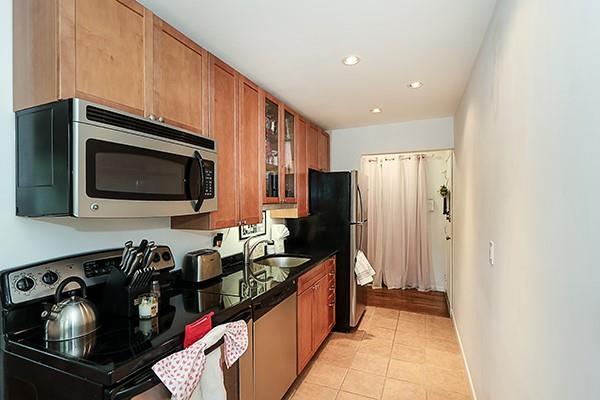 2449 Union Blvd Unit 24A, Islip, NY 11751 - kitchen with appliances with stainless steel finishes, dark countertops, brown cabinetry, glass insert cabinets, and light tile patterned floors