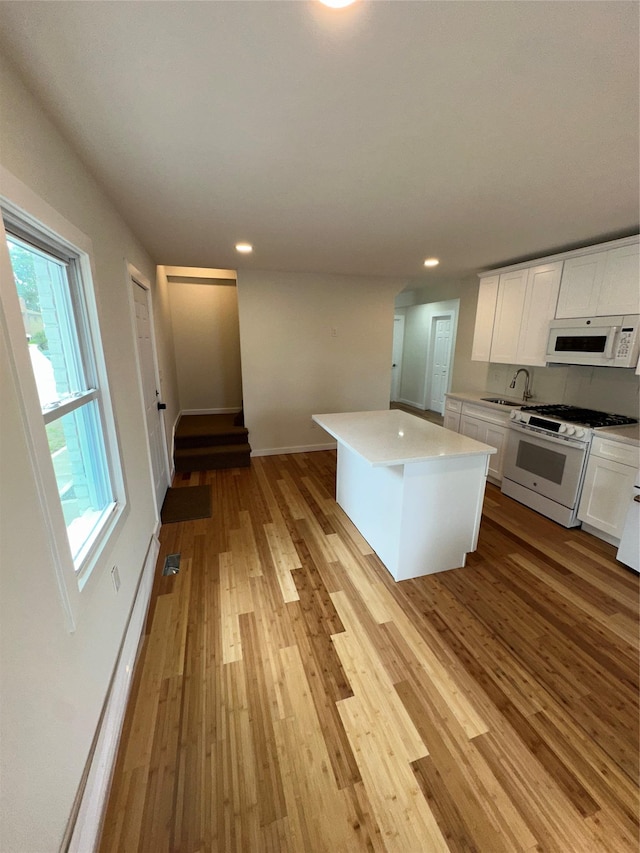 84 Windsor, Hempstead, NY 11550 - kitchen featuring white appliances, a sink, light wood-style flooring, white cabinets, and a center island