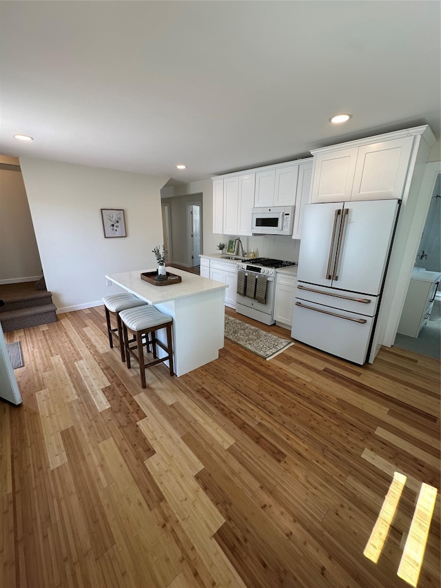 84 Windsor, Hempstead, NY 11550 - kitchen featuring white appliances, light wood-type flooring, recessed lighting, white cabinetry, and a kitchen island