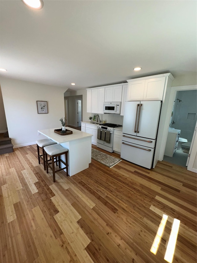 84 Windsor, Hempstead, NY 11550 - kitchen featuring white appliances, recessed lighting, light wood-style floors, white cabinets, and a kitchen breakfast bar
