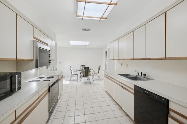 15 Augusta Ln, Manhasset, NY 11030 - kitchen featuring black appliances, a skylight, light countertops, light tile patterned floors, and white cabinets