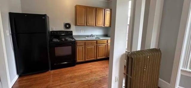 13 Hooker Ave, Poughkeepsie, NY 12601 - kitchen with black appliances, radiator heating unit, light wood finished floors, light countertops, and brown cabinetry