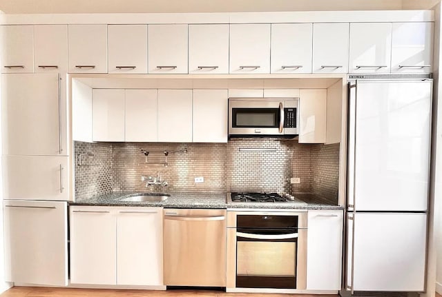 2728 Thomson Ave Unit 434, Long Island City, NY 11101 - kitchen featuring appliances with stainless steel finishes, white cabinets, dark stone counters, backsplash, and a sink