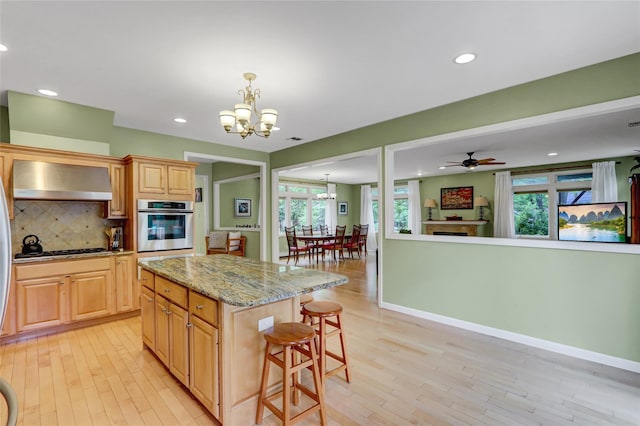 23 Knox Ave, Stony Brook, NY 11790 - kitchen featuring oven, a chandelier, wall chimney exhaust hood, a kitchen bar, and light wood finished floors