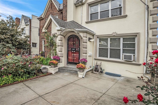 53-42 63rd St, Maspeth, NY 11378 - view of exterior entry with stucco siding, cooling unit, and roof with shingles