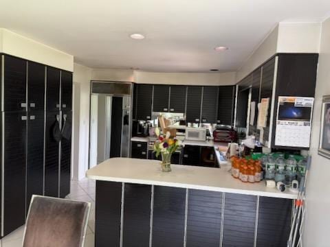 1055 Melissa Ln, North Bellmore, NY 11710 - kitchen featuring a peninsula, dark cabinetry, light countertops, light tile patterned floors, and white microwave