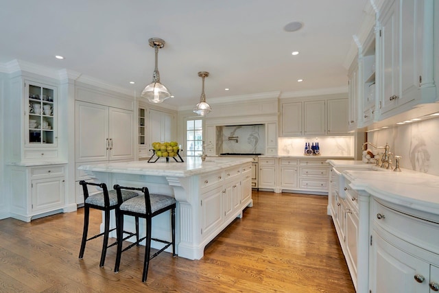 191 Elderfields Rd, Manhasset, NY 11030 - kitchen with white cabinetry, ornamental molding, a breakfast bar area, glass insert cabinets, and light stone counters