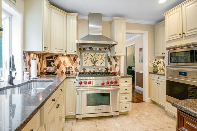100 Castle Rd, Chappaqua, NY 10514 - kitchen with cream cabinetry, wall chimney exhaust hood, stainless steel appliances, a sink, and dark stone counters