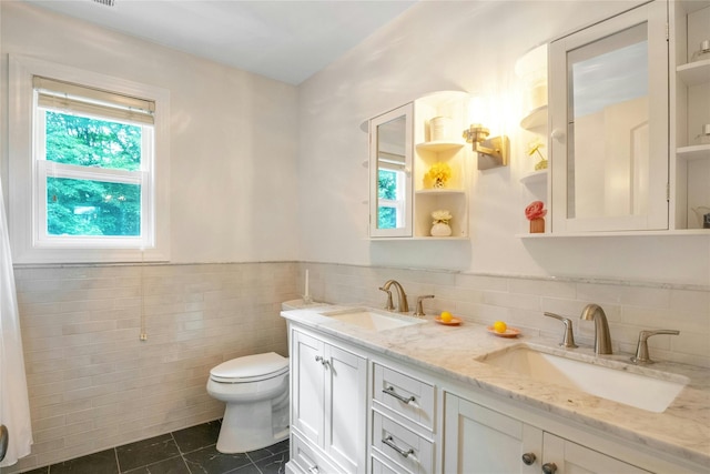 100 Castle Rd, Chappaqua, NY 10514 - bathroom featuring tile patterned floors, toilet, double vanity, tile walls, and a wainscoted wall