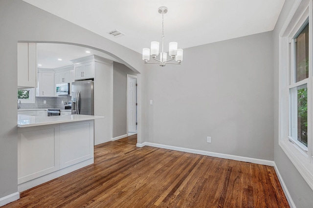 116 Amsterdam Ave, West Babylon, NY 11704 - unfurnished dining area featuring arched walkways, dark wood finished floors, a chandelier, and baseboards