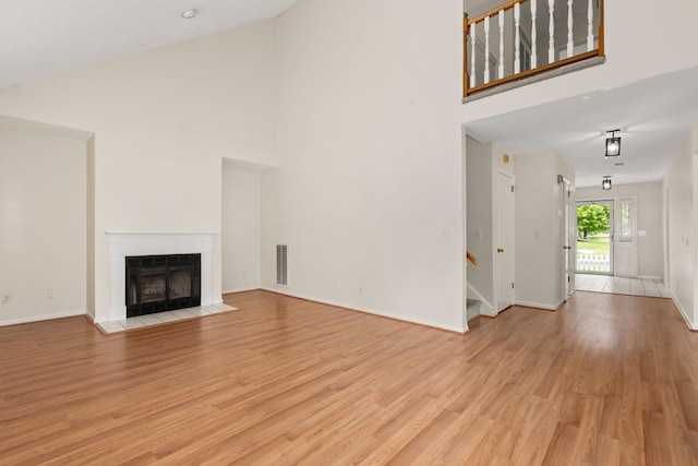 19 Cushing Grn S, Pawling, NY 12564 - unfurnished living room with high vaulted ceiling, light wood finished floors, baseboards, a fireplace with flush hearth, and stairway