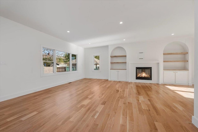 118 Broadway, Massapequa Park, NY 11762 - unfurnished living room featuring built in shelves, recessed lighting, light wood-style floors, a glass covered fireplace, and baseboards