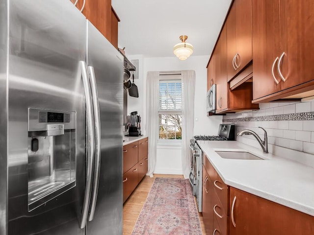 525 W 238th St Unit 1L, Bronx, NY 10463 - kitchen featuring appliances with stainless steel finishes, a sink, brown cabinets, light wood-style flooring, and tasteful backsplash