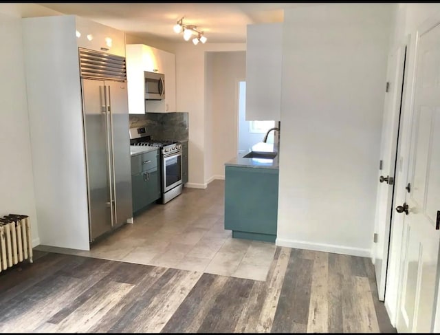 75-09 60th Pl, Glendale, NY 11385 - kitchen with appliances with stainless steel finishes, a sink, backsplash, radiator heating unit, and light wood-style flooring