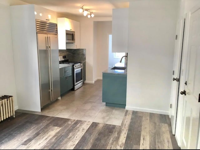 75-09 60th Pl, Glendale, NY 11385 - kitchen featuring appliances with stainless steel finishes, radiator heating unit, a sink, decorative backsplash, and light wood-style floors