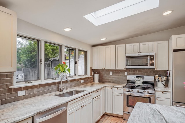 215 Lyman Rd, East Patchogue, NY 11772 - kitchen with appliances with stainless steel finishes, a sink, a skylight, light stone countertops, and lofted ceiling