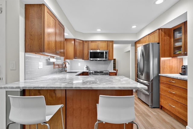 11 Robin Hood Rd, Montebello, NY 10901 - kitchen featuring appliances with stainless steel finishes, light wood-type flooring, a peninsula, backsplash, and brown cabinetry