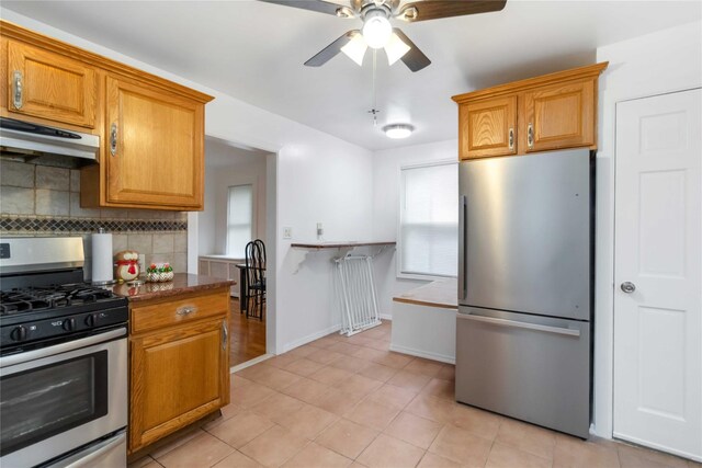 114-18 175th St, Addisleigh Park, NY 11434 - kitchen featuring appliances with stainless steel finishes, under cabinet range hood, tasteful backsplash, ceiling fan, and brown cabinets