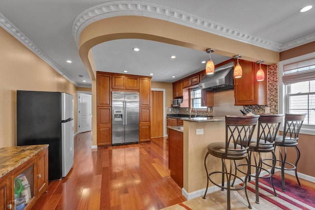 90 Milford St, Brooklyn, NY 11208 - kitchen with stainless steel appliances, a peninsula, brown cabinetry, crown molding, and hardwood / wood-style floors