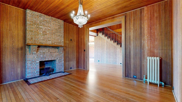 150 Senix Ave, Center Moriches, NY 11934 - unfurnished living room featuring radiator, a chandelier, hardwood / wood-style flooring, wooden walls, and stairs