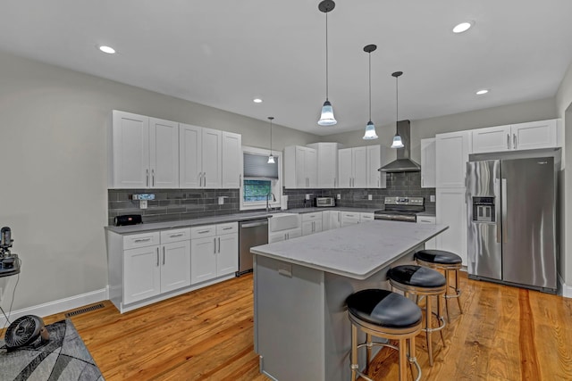 11 Fieldstone Ct, Highland, NY 12528 - kitchen featuring appliances with stainless steel finishes, wall chimney exhaust hood, decorative backsplash, a kitchen island, and light wood-type flooring