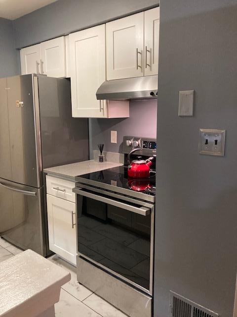 615 Broadway Unit 11, Amityville, NY 11701 - kitchen with stainless steel appliances, under cabinet range hood, white cabinets, and light marble finish floors