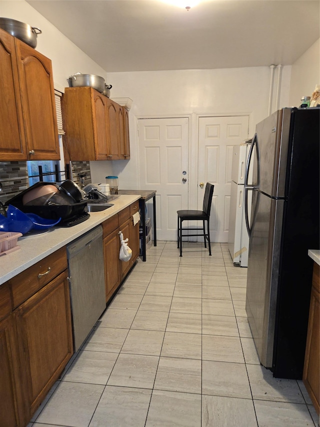 731 E 218th St, Bronx, NY 10467 - kitchen with appliances with stainless steel finishes, light countertops, light tile patterned floors, backsplash, and brown cabinetry