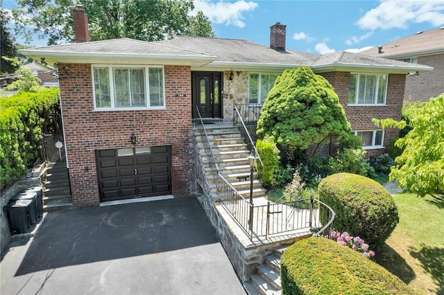 156 Valentine St, Yonkers, NY 10704 - view of front of house with a chimney, asphalt driveway, a garage, brick siding, and stairway