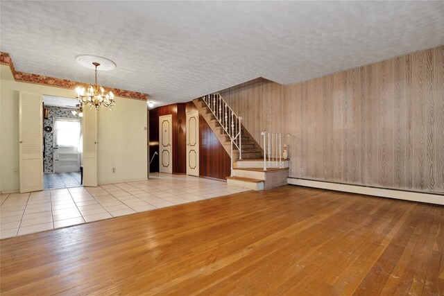 69-14 61st Rd, Middle Village, NY 11379 - unfurnished living room featuring a chandelier, wood finished floors, baseboard heating, stairway, and wood walls
