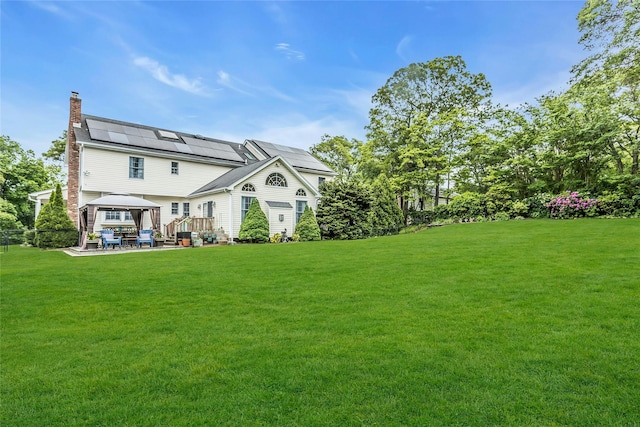16 Abbey Ln, East Setauket, NY 11733 - rear view of house featuring a gazebo, a chimney, solar panels, a yard, and a patio area