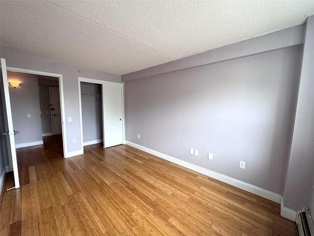 221 Bch 80th St Unit 2J, Rockaway Beach, NY 11693 - unfurnished bedroom with baseboard heating, baseboards, light wood finished floors, a textured ceiling, and a closet