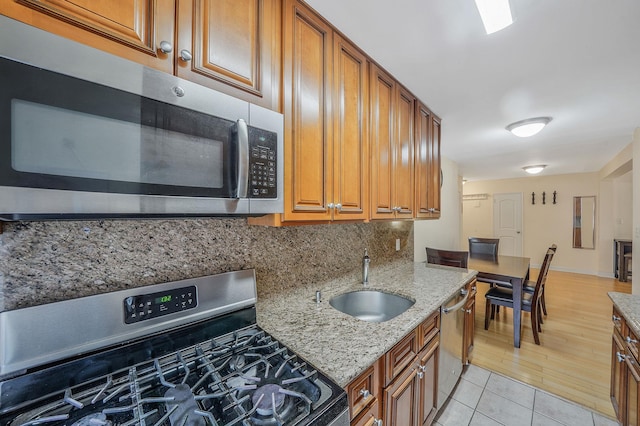 103-26 68th Ave Unit 2E, Forest Hills, NY 11375 - kitchen featuring appliances with stainless steel finishes, a sink, tasteful backsplash, brown cabinets, and light stone countertops