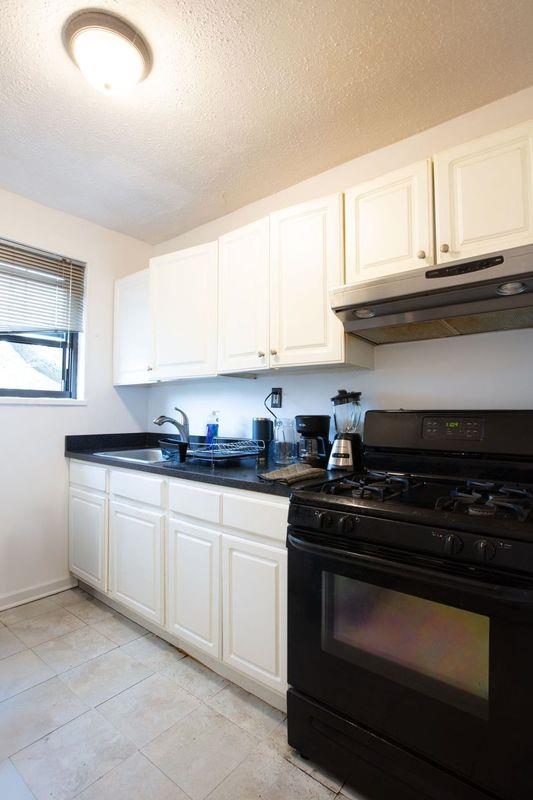 67-89 136th St Unit A, Kew Garden Hills, NY 11367 - kitchen with black range with gas cooktop, under cabinet range hood, a textured ceiling, white cabinetry, and a sink