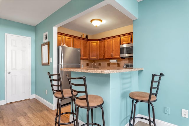 210 E Broadway Unit 1D, Long Beach, NY 11561 - kitchen featuring appliances with stainless steel finishes, a kitchen bar, brown cabinets, light wood-style flooring, and a peninsula