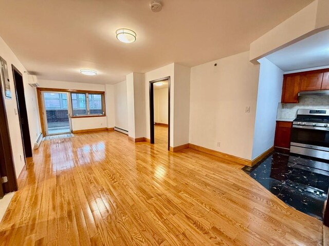 41-42 College Point Blvd Unit 3E, Flushing, NY 11355 - unfurnished living room with light wood finished floors, baseboard heating, an AC wall unit, and baseboards