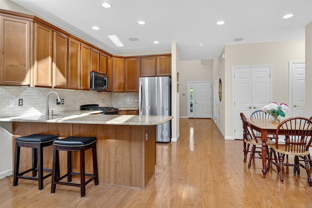 12 Miro Pl Unit 31, Port Washington, NY 11050 - kitchen featuring appliances with stainless steel finishes, a peninsula, brown cabinetry, tasteful backsplash, and light stone counters