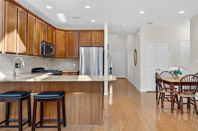 12 Miro Pl Unit 31, Port Washington, NY 11050 - kitchen with stainless steel appliances, a peninsula, brown cabinets, tasteful backsplash, and recessed lighting