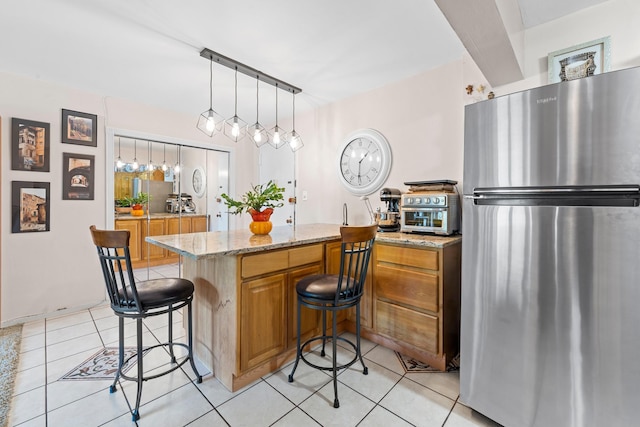 68-20 Selfridge St Unit 2F, Forest Hills, NY 11375 - kitchen with freestanding refrigerator, a kitchen bar, light tile patterned floors, light stone countertops, and brown cabinetry