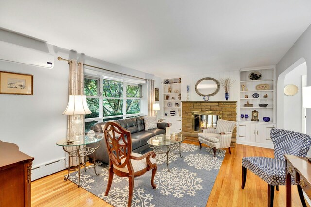 7 Woods Rd, Locust Valley, NY 11560 - living area with wood finished floors, built in features, a stone fireplace, a wall mounted AC, and a baseboard radiator