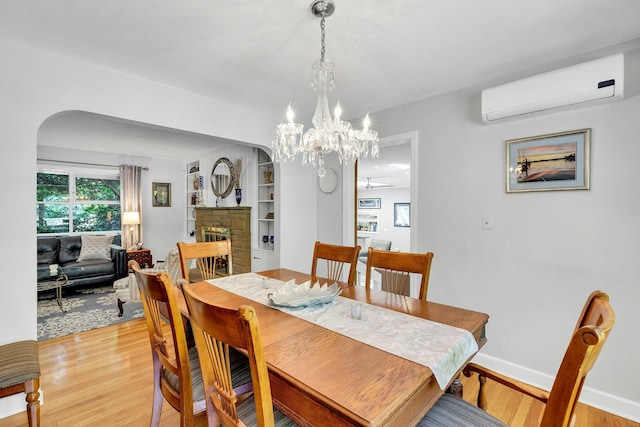 7 Woods Rd, Locust Valley, NY 11560 - dining area featuring arched walkways, a wall unit AC, light wood-style flooring, a fireplace, and a chandelier