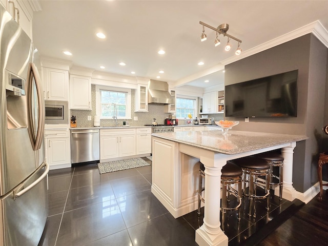 352 Mill Spring Rd, Manhasset, NY 11030 - kitchen featuring appliances with stainless steel finishes, wall chimney range hood, plenty of natural light, light stone countertops, and crown molding