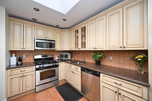 206-05 Emily Rd Unit 6U, Bayside, NY 11360 - kitchen featuring cream cabinetry, appliances with stainless steel finishes, light tile patterned floors, backsplash, and glass insert cabinets
