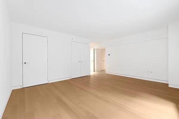 135 W 52nd St Unit 8D, New York Manhattan, NY 10019 - unfurnished bedroom featuring wood finished floors and two closets