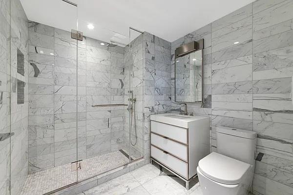 135 W 52nd St Unit 8D, New York Manhattan, NY 10019 - bathroom with toilet, vanity, a marble finish shower, tile walls, and marble finish flooring